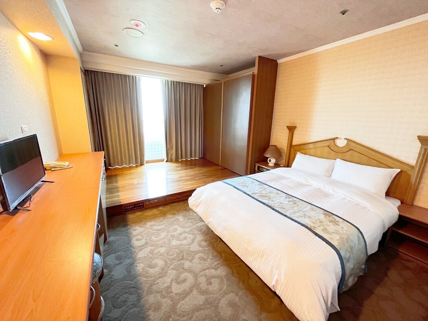 A hotel room with a bed, a desk, a television, and a view of the outside.