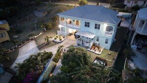 A two-story house with a balcony, surrounded by a well-maintained garden with various plants and a pathway leading to the entrance. - Breathtaking views 5min from the beach! (Old Road Village)