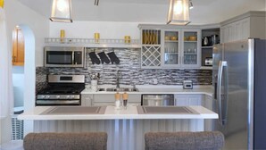 A modern kitchen with a central island, stainless steel appliances, and pendant lighting. - Breathtaking views 5min from the beach! (Old Road Village)