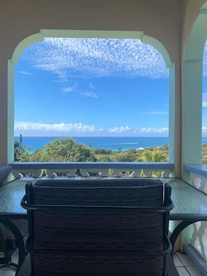 Un balcon avec vue sur l’océan et la verdure.