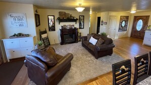 A spacious living room with a fireplace, a white cabinet, and a brown leather sofa. - Beautiful Getaway Near Park City with Private Hot Tub (Kamas)