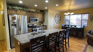 A kitchen with a central island, stainless steel appliances, wooden cabinets, and a dining area with a chandelier. - Beautiful Getaway Near Park City with Private Hot Tub (Kamas)