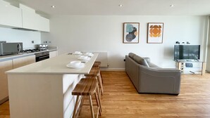 Een moderne keuken met een centraal eiland, houten barkrukken, een grijze bank en een flatscreen televisie.