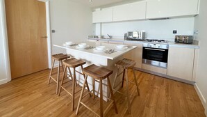 Een moderne keuken met een centraal eiland, barstoelen, een inbouwoven en witte kastjes.
