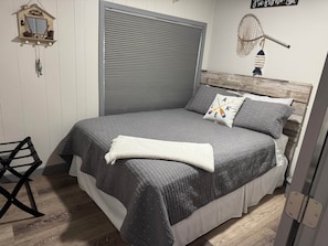 A bedroom with a bed, a window with blinds, a wall-mounted shelf with decorative items, and a wall decoration of a fishing net.