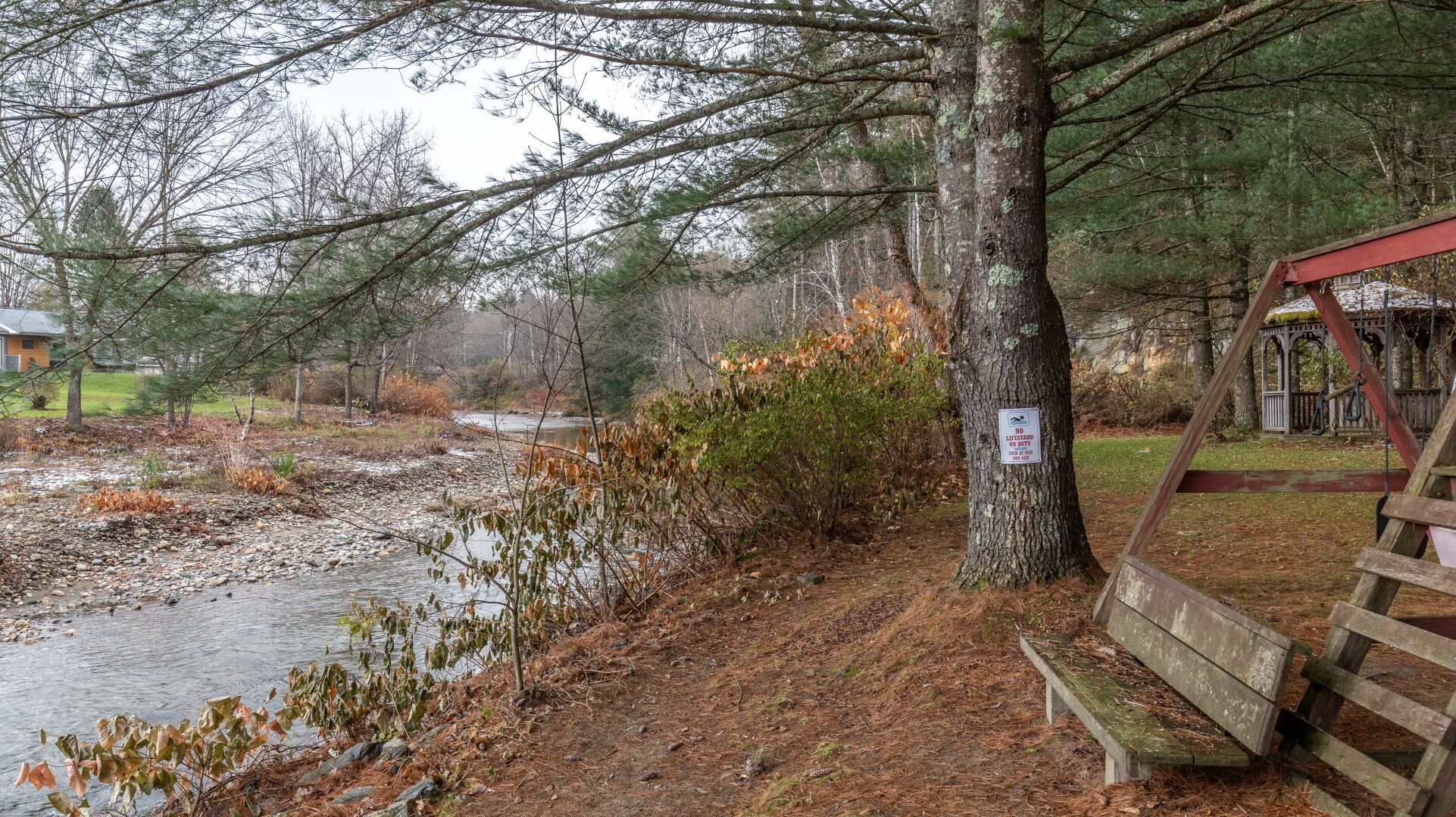 A wooden bench by a riverbank with a no swimming sign on a tree.
