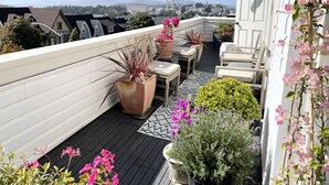 Terraza en la azotea con plantas en macetas, mobiliario exterior y vistas a la ciudad.