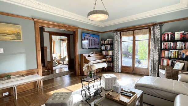 Una sala de estar amplia con un piano, una estantería y un gran ventanal con cortinas.