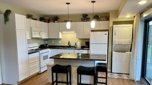 Una cocina moderna con armarios blancos, una isla central con taburetes, un refrigerador y una estufa.