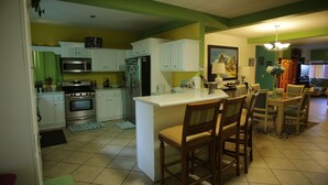 A kitchen with white cabinets, a central island with bar stools, and a dining area with a table and chairs. - Trojan Beach House (Ensenada)