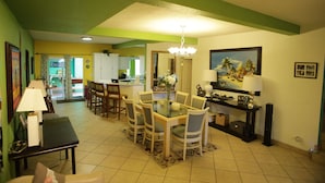 A dining area with a glass table, chairs, a chandelier, and a painting on the wall. - Trojan Beach House (Ensenada)