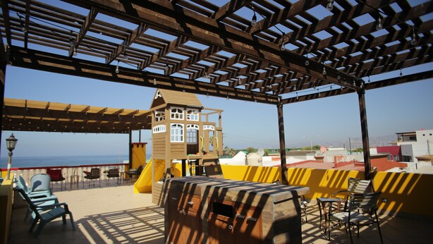 A covered outdoor area with a wooden play structure, seating, and a view of the sea. - Trojan Beach House (Ensenada)
