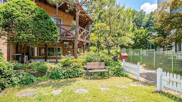 Ein Holthaus mit Balkon, umgeben von einem Garten mit Bank und Zaun.