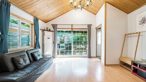 A spacious room with a wooden ceiling, a leather sofa, a large sliding glass door leading to an outdoor area, and a wooden bench. - Gapyeong Ojeupension (Gapyeong)
