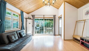 Una habitación amplia con techo de madera, sofá de cuero, un gran ventanal corredero que da a un espacio exterior y un banco de madera.