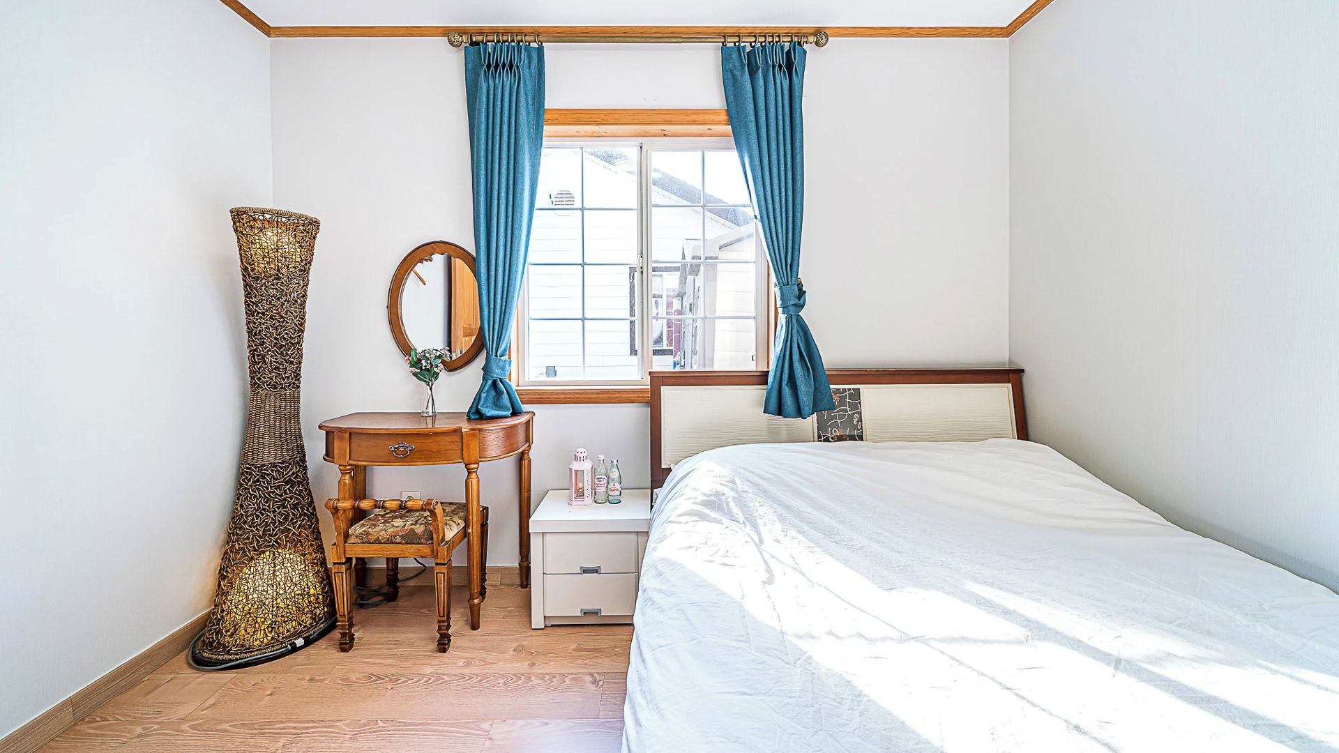 A bedroom with a bed, a bedside table, a mirror, a chair, and a large vase.