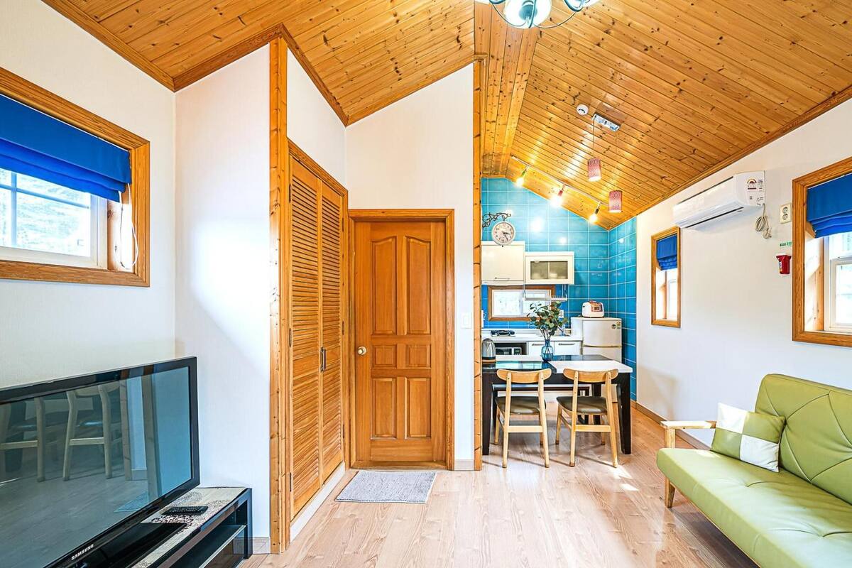 Un espace de vie compact doté d’un plafond en bois, d’un coin repas avec une table et des chaises, d’un canapé vert et d’un téléviseur.