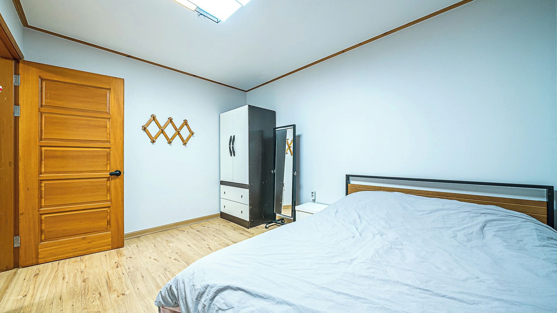 A bedroom with a wooden door, a wardrobe, a bed with a white bedspread, and a mirror on the wall.