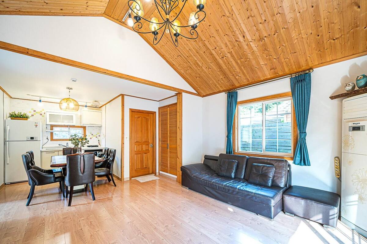 Un vaste espace de vie doté d’un plafond en bois, un coin repas avec une table et des chaises, un canapé et une grande fenêtre agrémentée de rideaux.