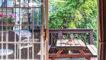 Una terraza de madera con una mesa lista para una comida, una parrilla y vistas de un jardín a través de un ventanal.