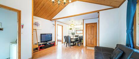 A spacious living area with a wooden ceiling, a television, a dining table with chairs, and a sofa.