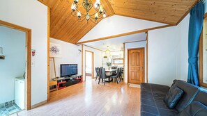 A spacious living area with a wooden ceiling, a television, a dining table with chairs, and a sofa. - Gapyeong Ojeupension (Gapyeong)
