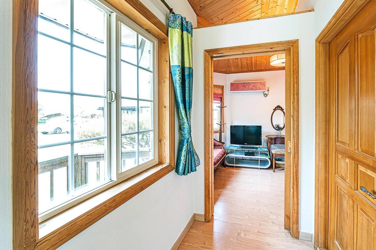 Un couloir avec une grande fenêtre, une porte en bois et un téléviseur à l’arrière-plan.