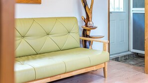 Ein grünes Sofa mit einer gepolsterten Rückenlehne, ein Holznachttisch mit einer Glasbowl und eine Holzskulptur.
