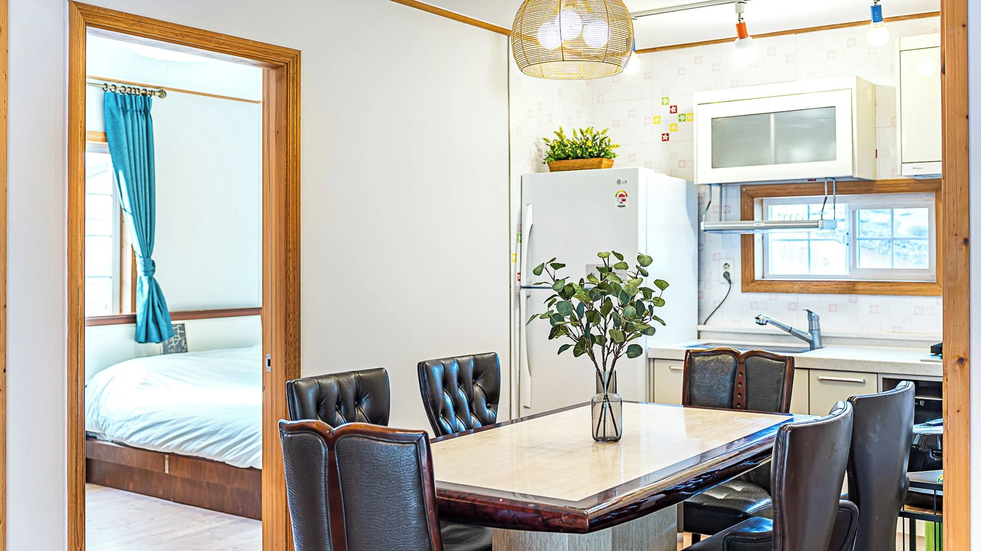 A modern room with a bed, a dining table with chairs, a kitchen area, and a large window with curtains.
