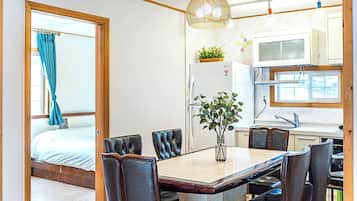 A modern room with a bed, a dining table with chairs, a kitchen area, and a large window with curtains.