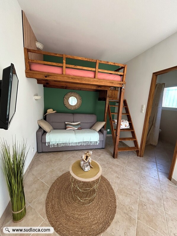A room with a bunk bed, a grey sofa, a decorative mirror, and a woven stool. - 30 m2 in a Villa - Grand Ajaccio (peri)