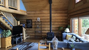 A log cabin interior with a wooden staircase, a fireplace, a sofa, and a dining table. - Cozy Custom Log Cabin Nestled within Mile High Estates (Logan Lake)