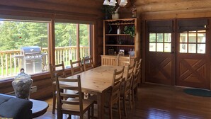 A wooden cabin interior with a dining table, chairs, a grill, and a bookshelf. - Cozy Custom Log Cabin Nestled within Mile High Estates (Logan Lake)