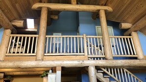 A wooden balcony with railings, a staircase, and a blue wall. - Cozy Custom Log Cabin Nestled within Mile High Estates (Logan Lake)