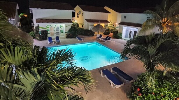 Zona de piscina amb gandules, una estora de palla i un edifici amb teulada de rajola vermella.