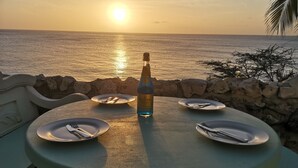 Una taula amb plats, coberts, una ampolla i vista al mar al capvespre.