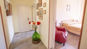 Un pasillo que conduce a un dormitorio con una cama, una silla y un florero con flores.