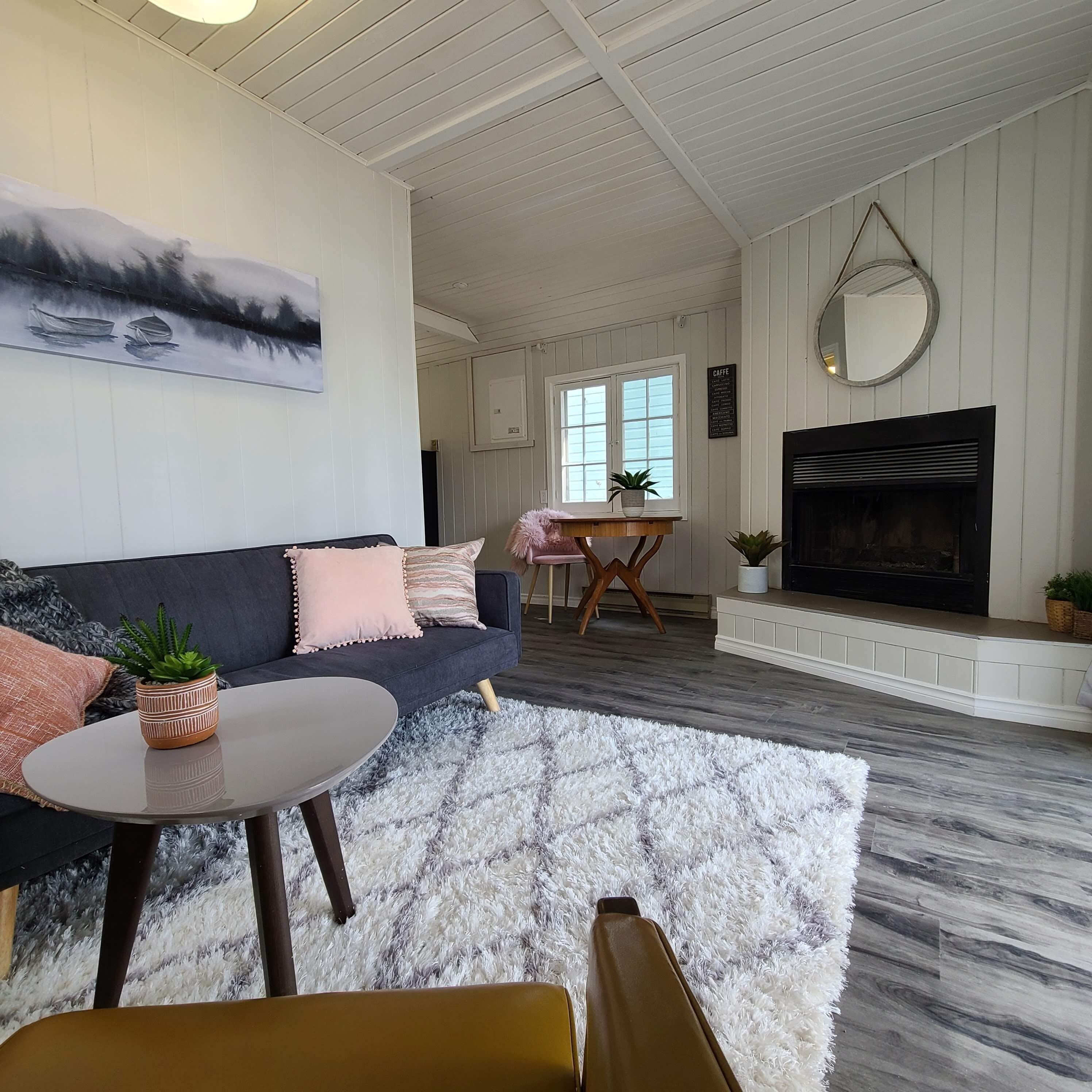 A living room with a sofa, coffee table, and a fireplace. There is a dining area in the background with a table and chairs.