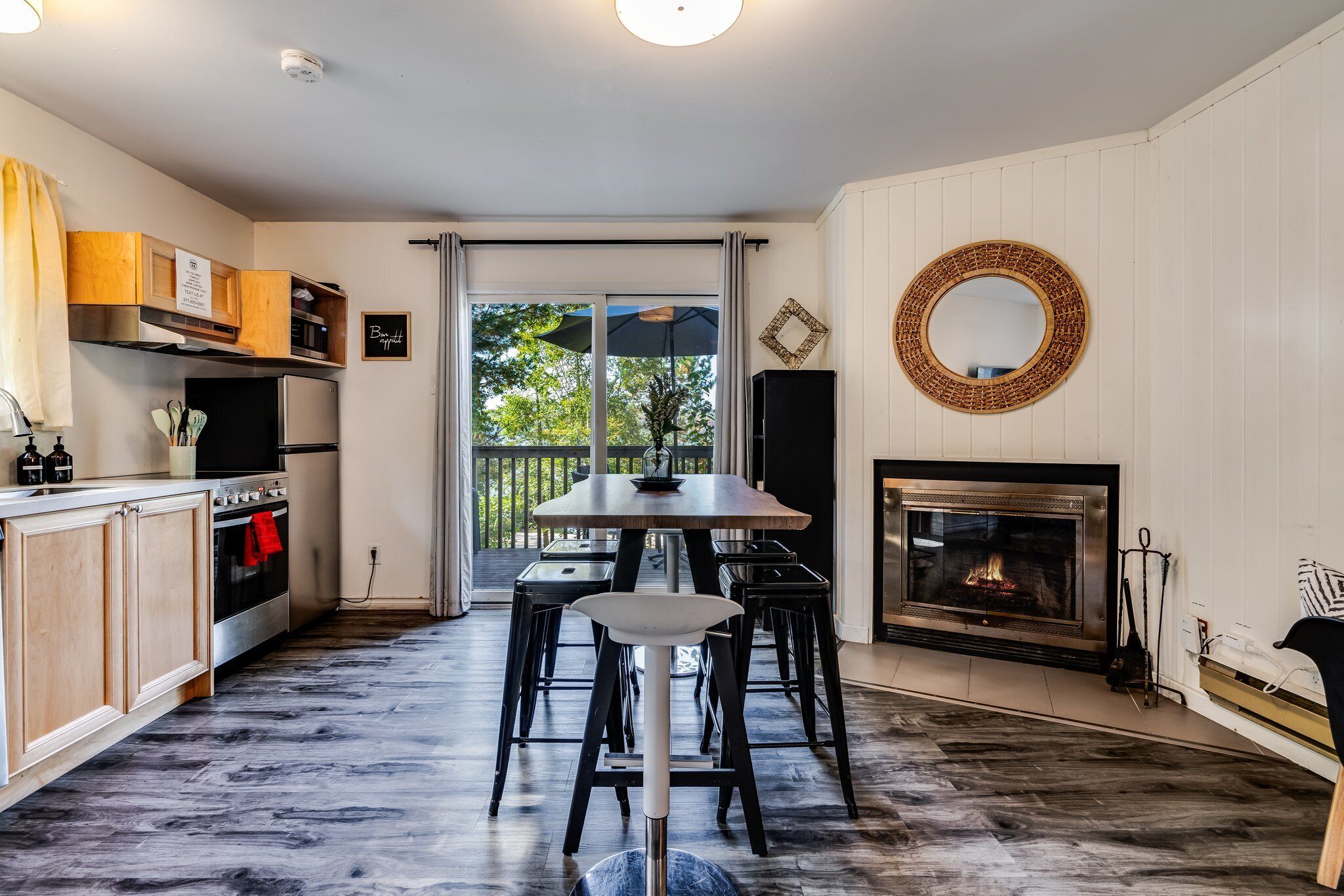 A modern kitchen with a dining area, a fireplace, and a view through the glass door.