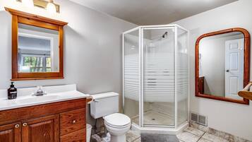 Un baño con tocador de madera, lavamanos blanco y ducha con mampara de vidrio.