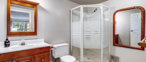 Un baño con tocador de madera, lavamanos blanco y ducha con mampara de vidrio.