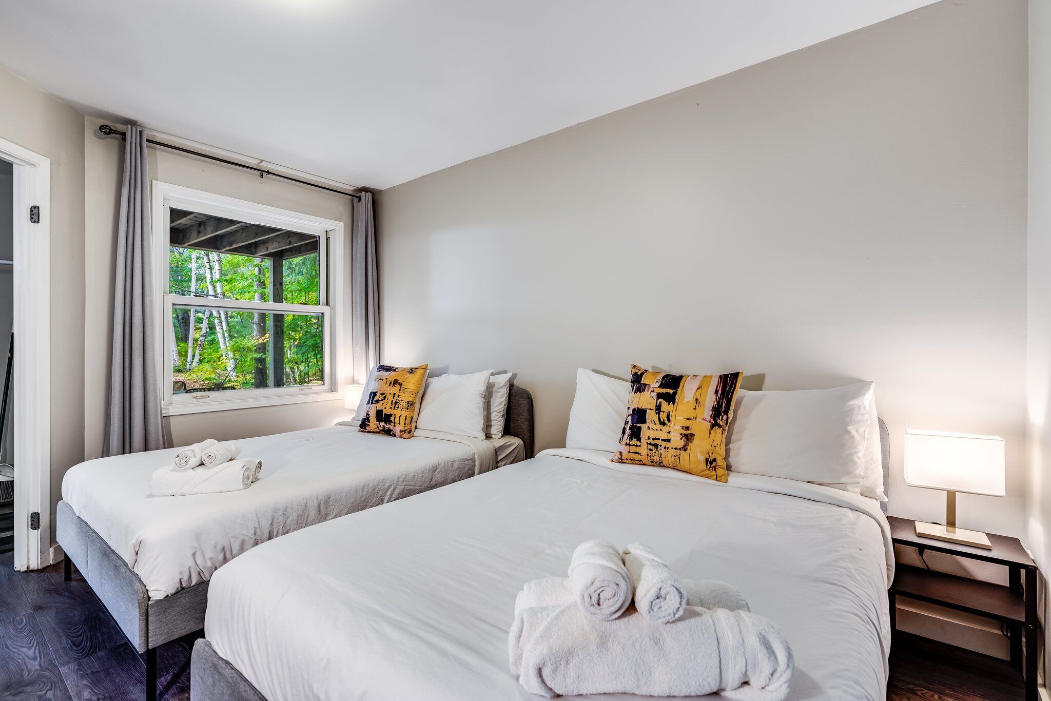 Una habitación de hotel con dos camas, una ventana que da a zonas verdes, una mesita de noche con lámpara y toallas sobre las camas.