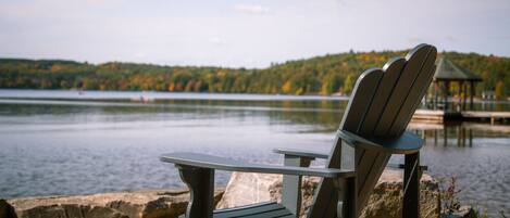 Una silla Adirondack mirando a un lago tranquilo, con una colina boscosa al fondo.
