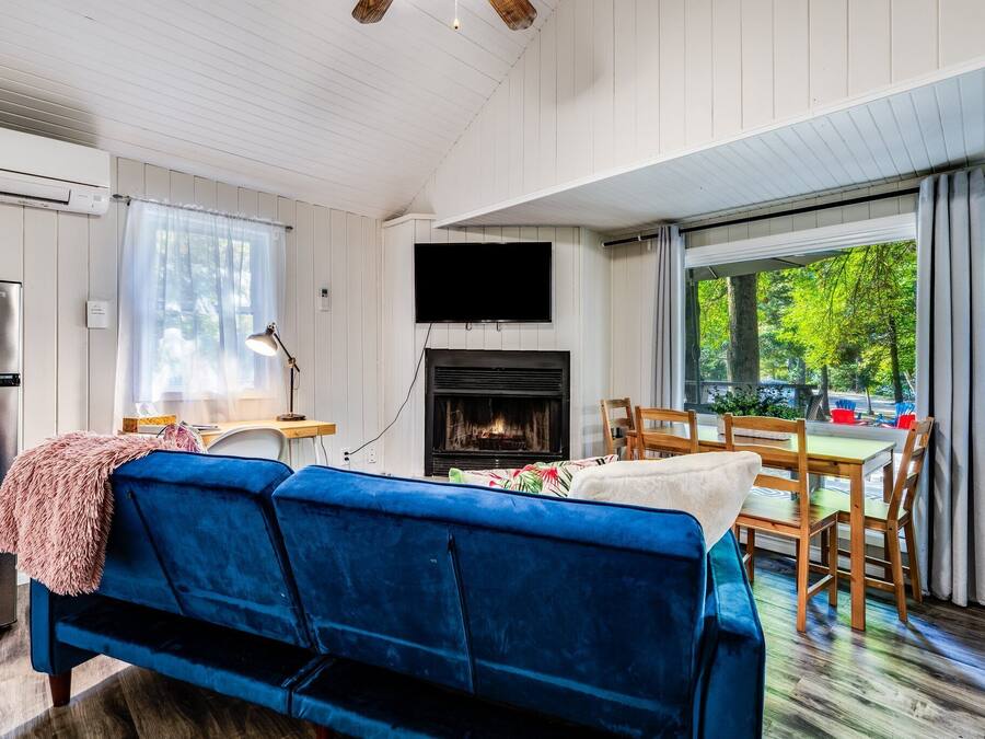 Een gezellige woonkamer met een blauwe bank, een open haard, een eettafel met stoelen en een aan de muur bevestigde televisie.