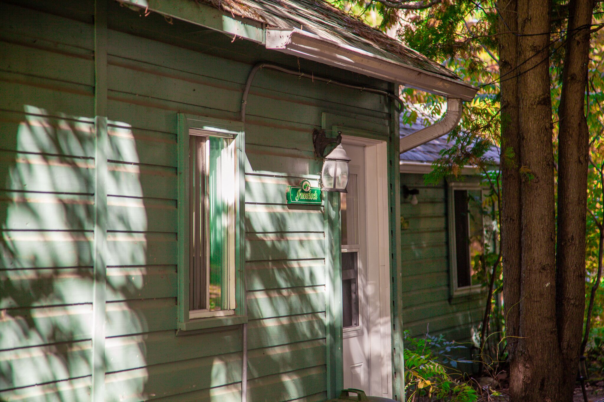 Una casa de madera verde con porche, una señal de calle y un poste de luz.