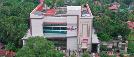 Un centro comercial grande con un llamativo letrero que dice 'Big Mall', rodeado de abundante vegetación y edificios residenciales.