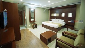 A hotel room with a large bed, a wooden headboard, a TV, a desk, and a chair. - Big Mall Residency (Hosdurg)