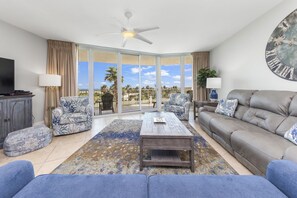 Relax in this stylish living room with a large flat-screen TV, comfortable seating, and a beautiful view of palm trees.