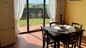 A dining area with a table, chairs, a television, and a view of a garden through a glass door.