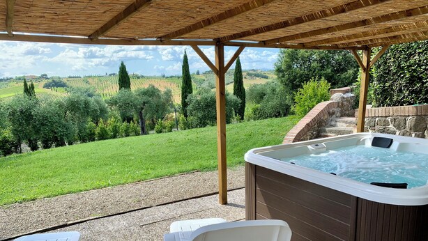 A hot tub under a wooden pergola with a view of a vineyard and rolling hills.